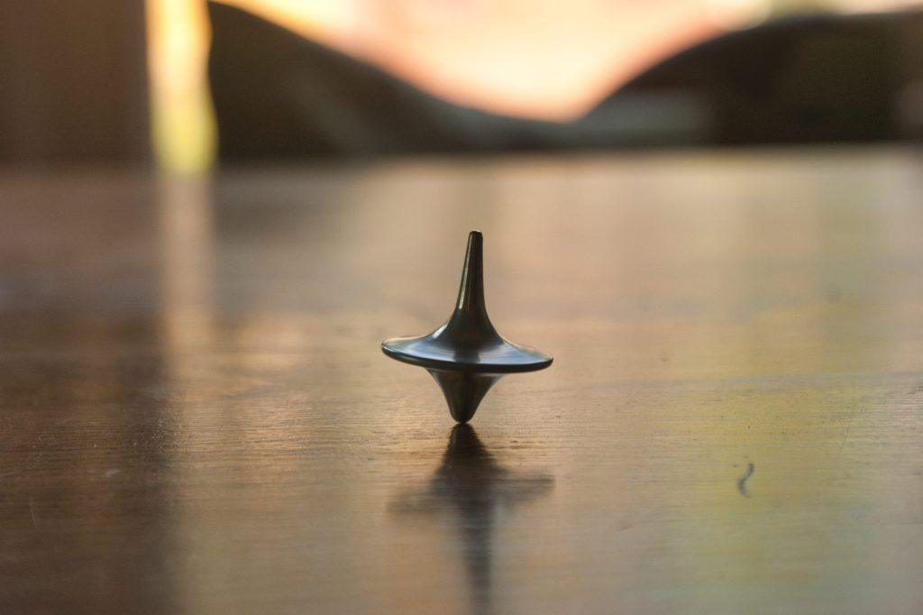 A metal spinning top in motion on a wooden table with a soft, blurred background.