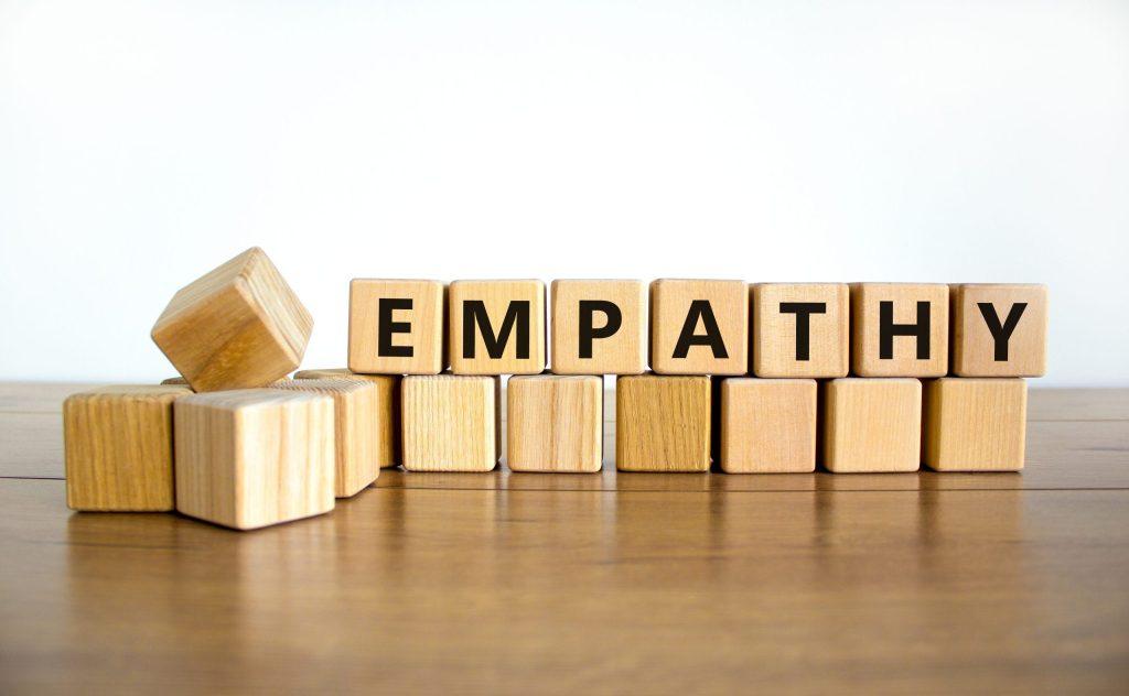 Wooden blocks spelling the word “EMPATHY” on a wooden table with a plain white background.